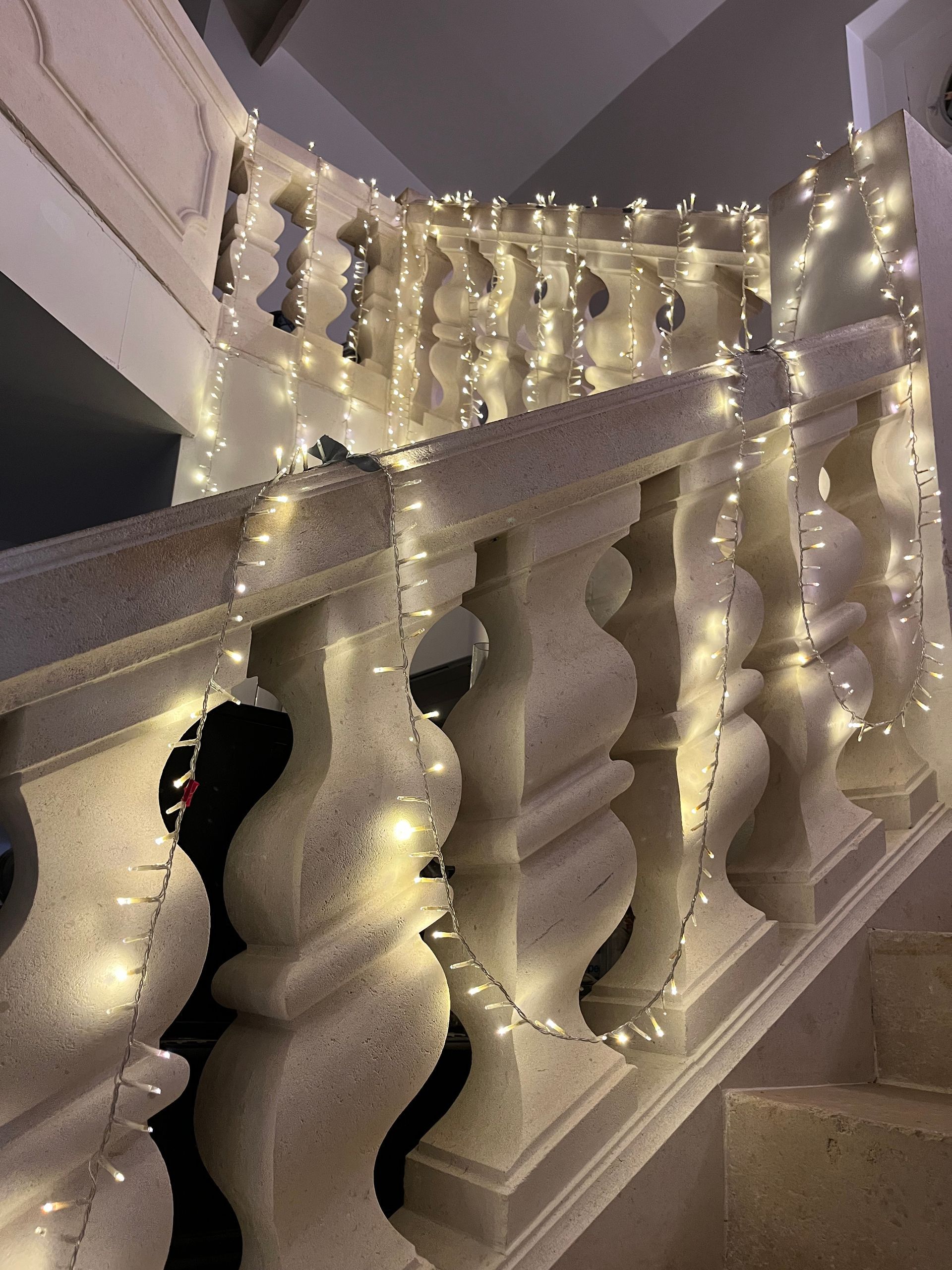 Rambarde d'escalier blanche ornée de guirlandes lumineuses blanc chaud dans un couloir incurvé