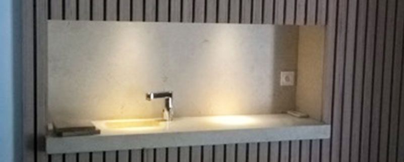 Un lavabo encastré dans une niche d'un mur en bois à lattes verticales. Un robinet et une prise d'eau sont visibles.