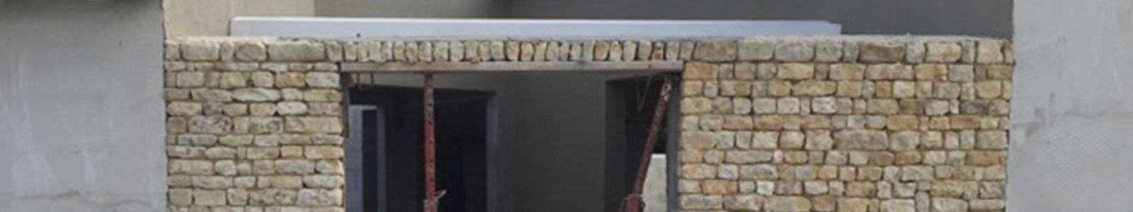 Une arche en briques brun clair, avec une structure en béton gris et un toit plat blanc.