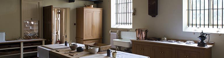 Intérieur d'une pièce avec fenêtres et tables. On y trouve une grande armoire et divers objets sur les tables.