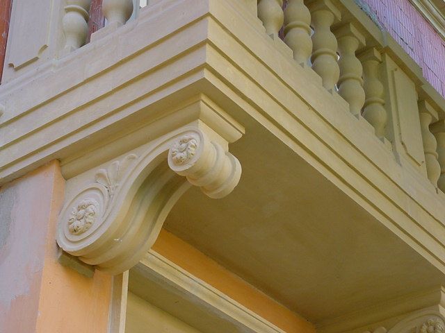 Détail d'un balcon en pierre beige orné de volutes et d'une balustrade.