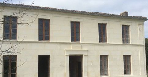 Bâtiment beige de deux étages avec des fenêtres rectangulaires et une porte centrale.