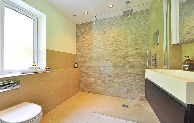 Salle de bains avec carrelage mural texturé beige, douche et meuble-lavabo suspendu. Fenêtre à gauche et toilettes.