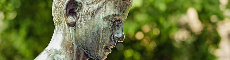 Gros plan sur la tête d'une statue en bronze, probablement celle d'un jeune homme, sur un fond vert flou.