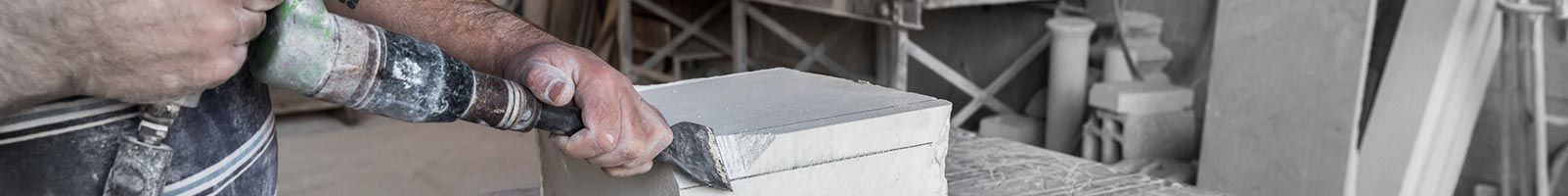 Une personne travaillant avec du ciment, tenant un outil à côté d'un bloc rectangulaire sur un chantier de construction.