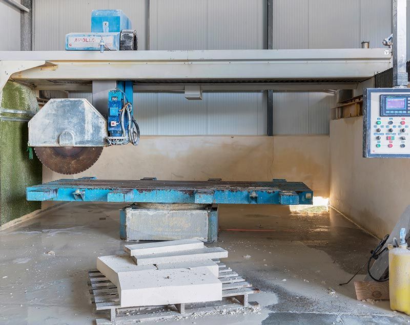 Machine de découpe de pierre dans une usine, en train de découper un bloc de pierre de couleur claire, avec panneau de commande.