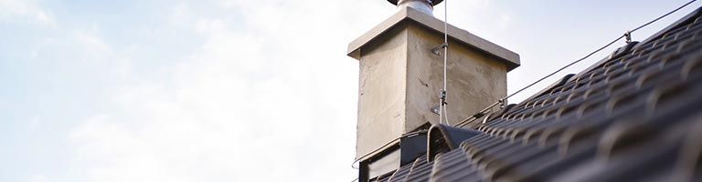 Une haute cheminée en béton sur un toit de tuiles se détachant sur un ciel lumineux.