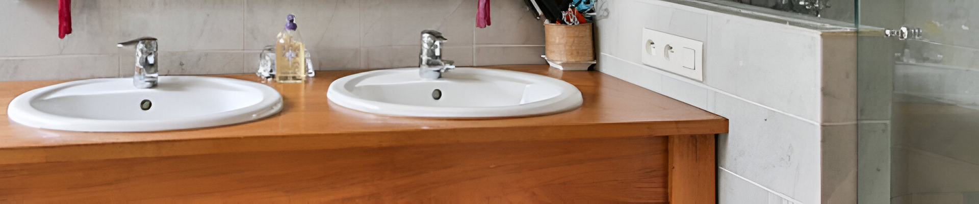 Meuble-lavabo de salle de bain avec deux lavabos blancs, comptoir en bois et mur carrelé gris.