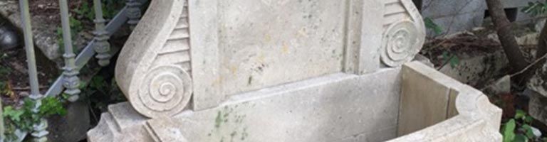 Fontaine en pierre ornée de volutes, possiblement en extérieur.