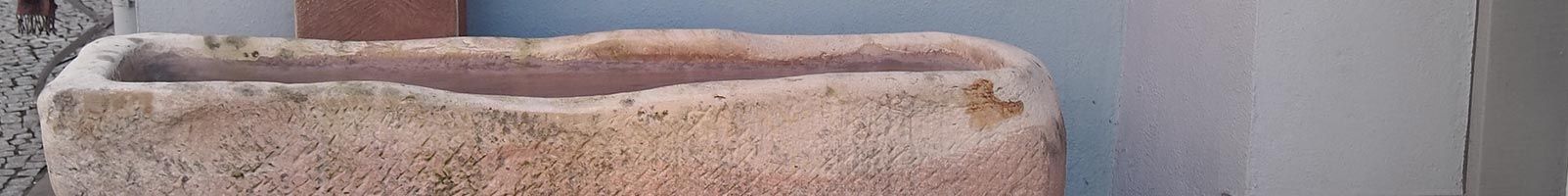 Une jardinière rectangulaire en pierre patinée, ouverte sur le dessus, se détache sur un fond aux tons neutres.