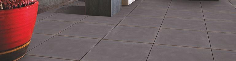 Sol carrelé gris foncé, un grand pot rouge à gauche et un mur sombre partiellement visible en arrière-plan.