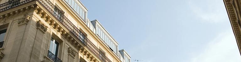 Façade du bâtiment ornée de sculptures et de fenêtres se détachant sur un ciel bleu.
