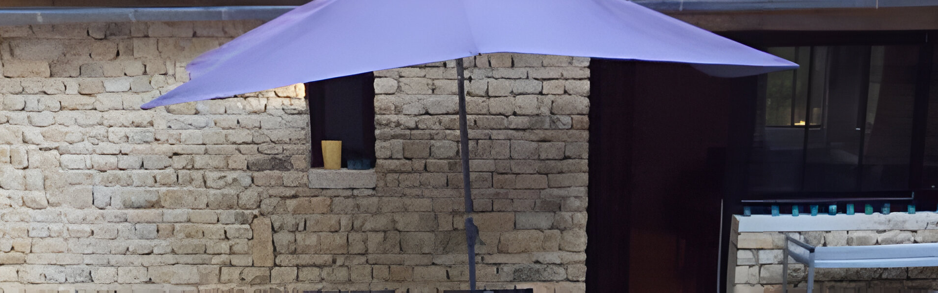 Un parapluie lilas est ouvert devant un mur de briques et une porte sombre.