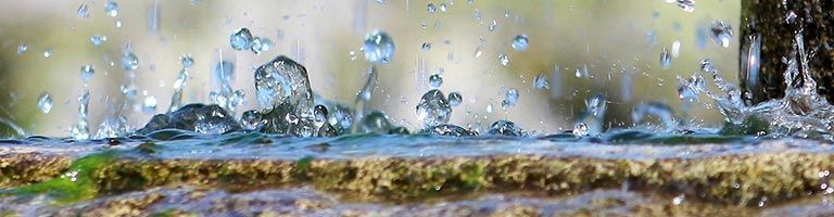 Des gouttelettes d'eau s'écrasent sur une surface moussue, sur un fond flou.