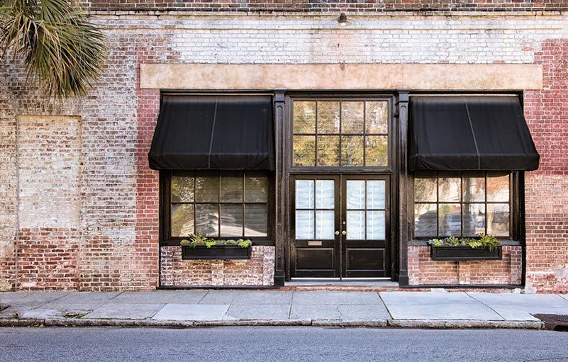 Façade de magasin avec auvents noirs et jardinières sur un bâtiment en briques.