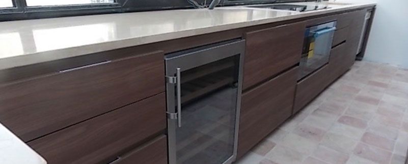 Une cuisine moderne avec des armoires en bois foncé, une cave à vin en acier inoxydable et un plan de travail clair.