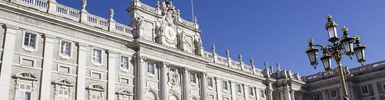 Extérieur du Palais Royal de Madrid sous un ciel bleu, avec un lampadaire décoratif.