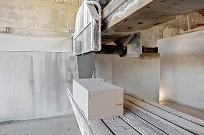 Un bloc de pierre est découpé par une grande scie industrielle dans un environnement d'usine aux tons clairs.