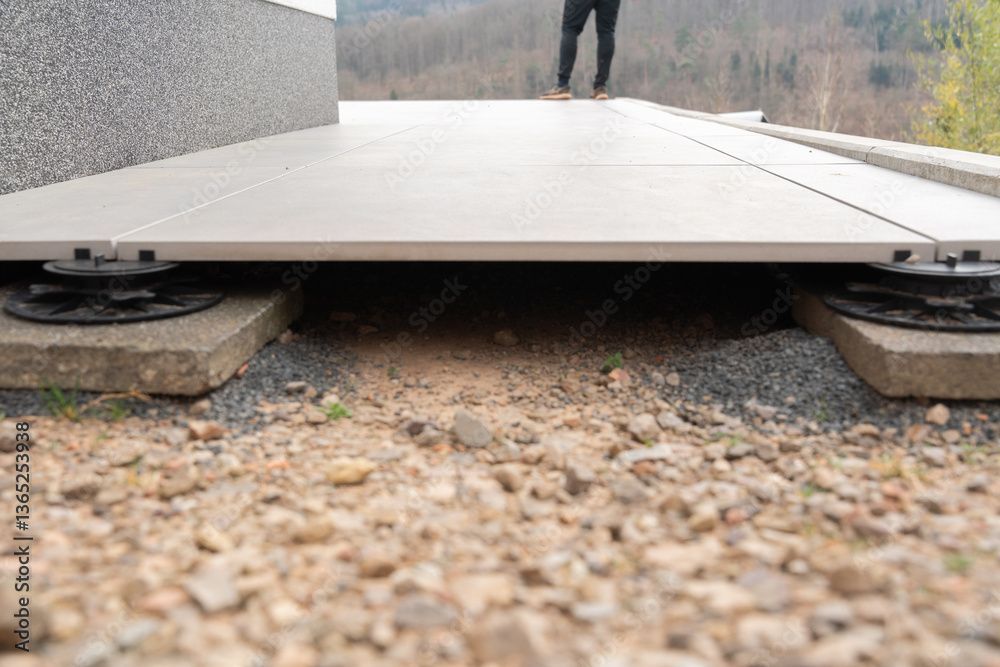 Une vue en contre-plongée montre de grands carreaux extérieurs installés sur des socles réglables reposant sur des dalles de béton recouvertes de gravier.
