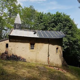 Chapelle en pierre avec toit d'ardoise, petit clocher et arbres environnants.
