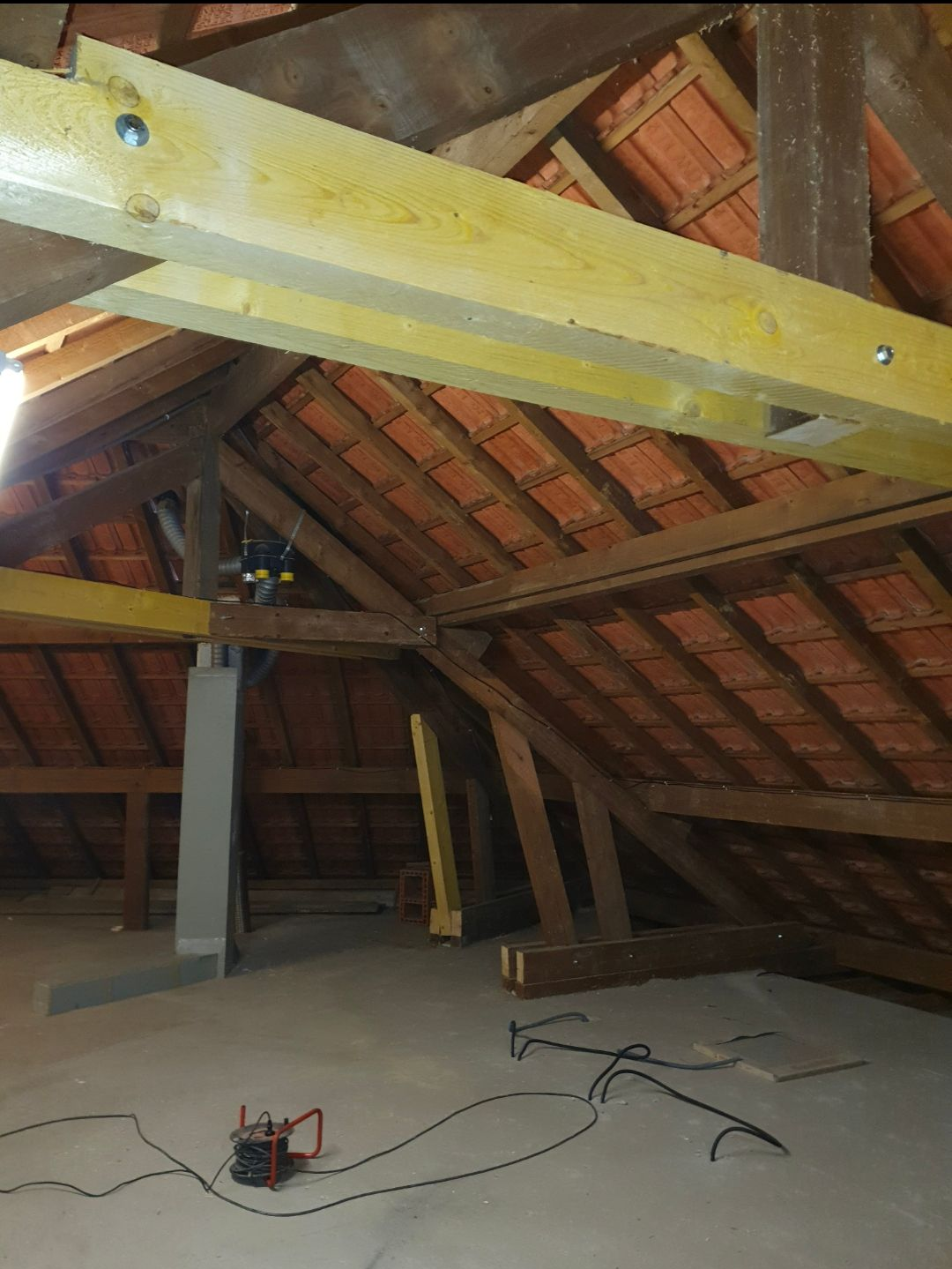 Intérieur du grenier avec poutres et chevrons apparents, nouveaux supports en bois et équipements au sol.