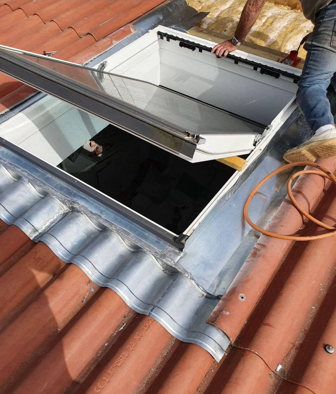 Puits de lumière ouvert sur un toit de tuiles. Une personne travaille sur la structure ; l’isolation est visible.