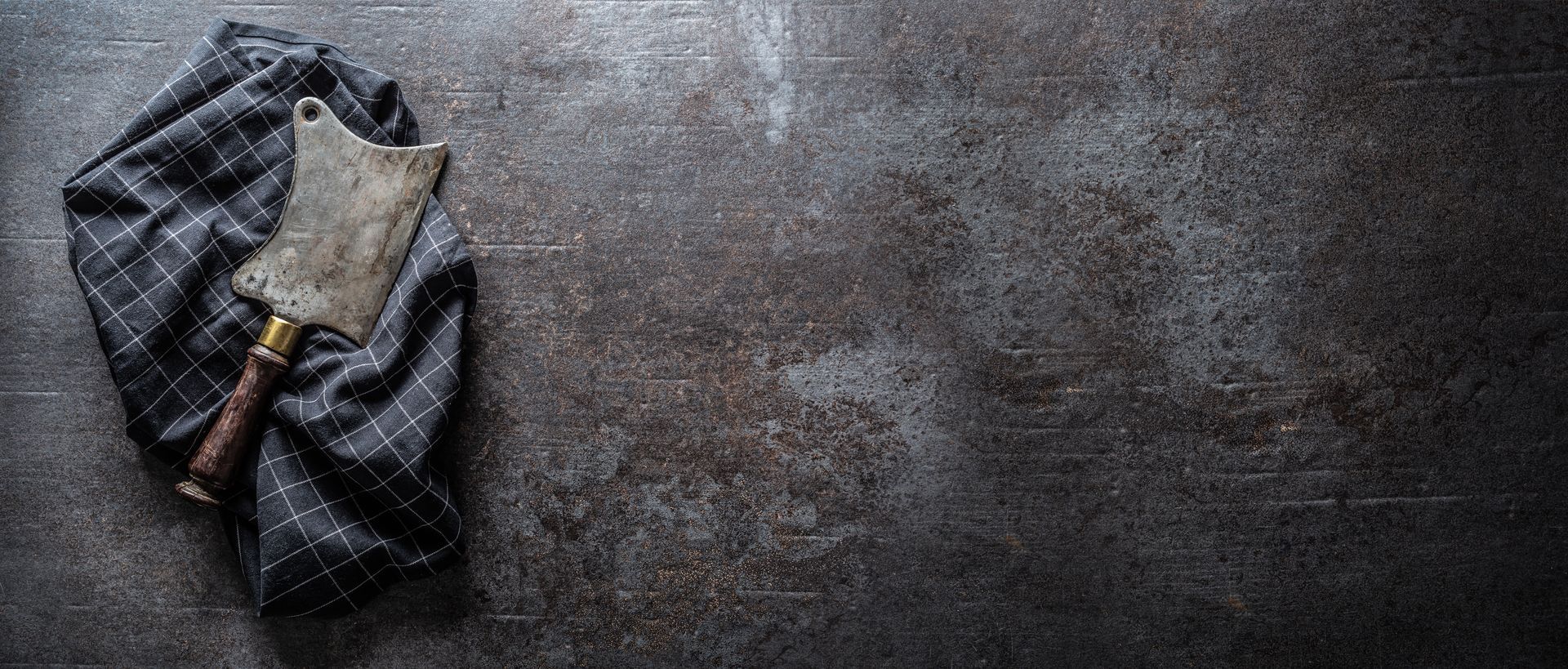 Couperet à viande sur un tissu à carreaux foncés sur une surface grise texturée et marbrée.