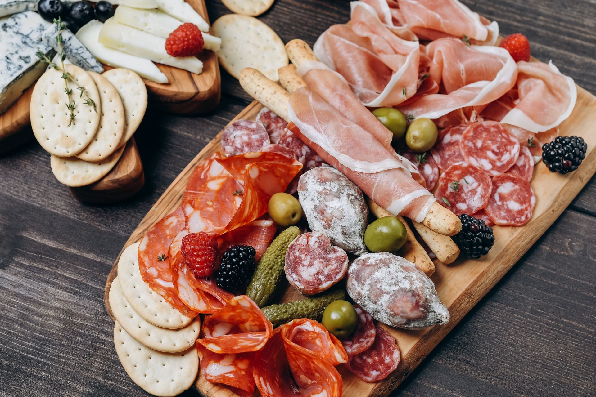 Planche de charcuterie avec viandes, fromages, craquelins, olives et baies disposés sur une surface en bois.