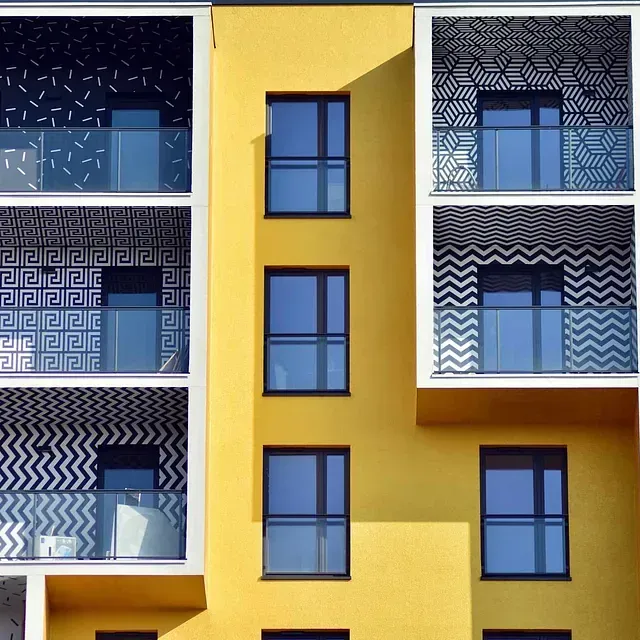 Edificio de apartamentos amarillo con balcones con dibujos geométricos y ventanas con marco azul.