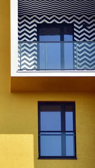 Fachada de edificio de color amarillo con una ventana y un balcón con toldo con estampado en zigzag.