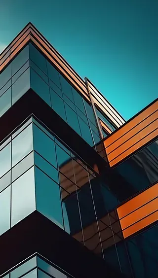 Exterior de un edificio moderno con ventanas de cristal y paneles naranjas contra un cielo azul. Vista en ángulo desde abajo.