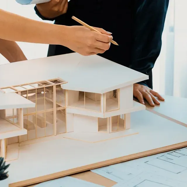 Dos personas discuten un modelo de una casa moderna, usando un lápiz para señalar una sección.