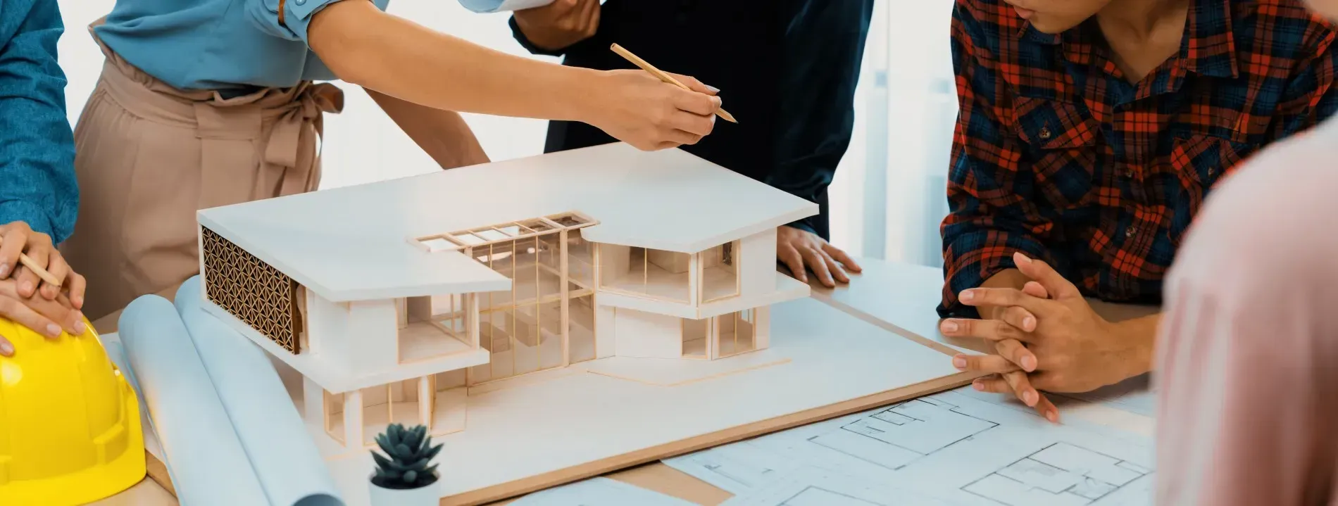 Arquitectos colaboran en la maqueta de un edificio. Personas con ropa informal examinan la estructura, con una persona señalando.