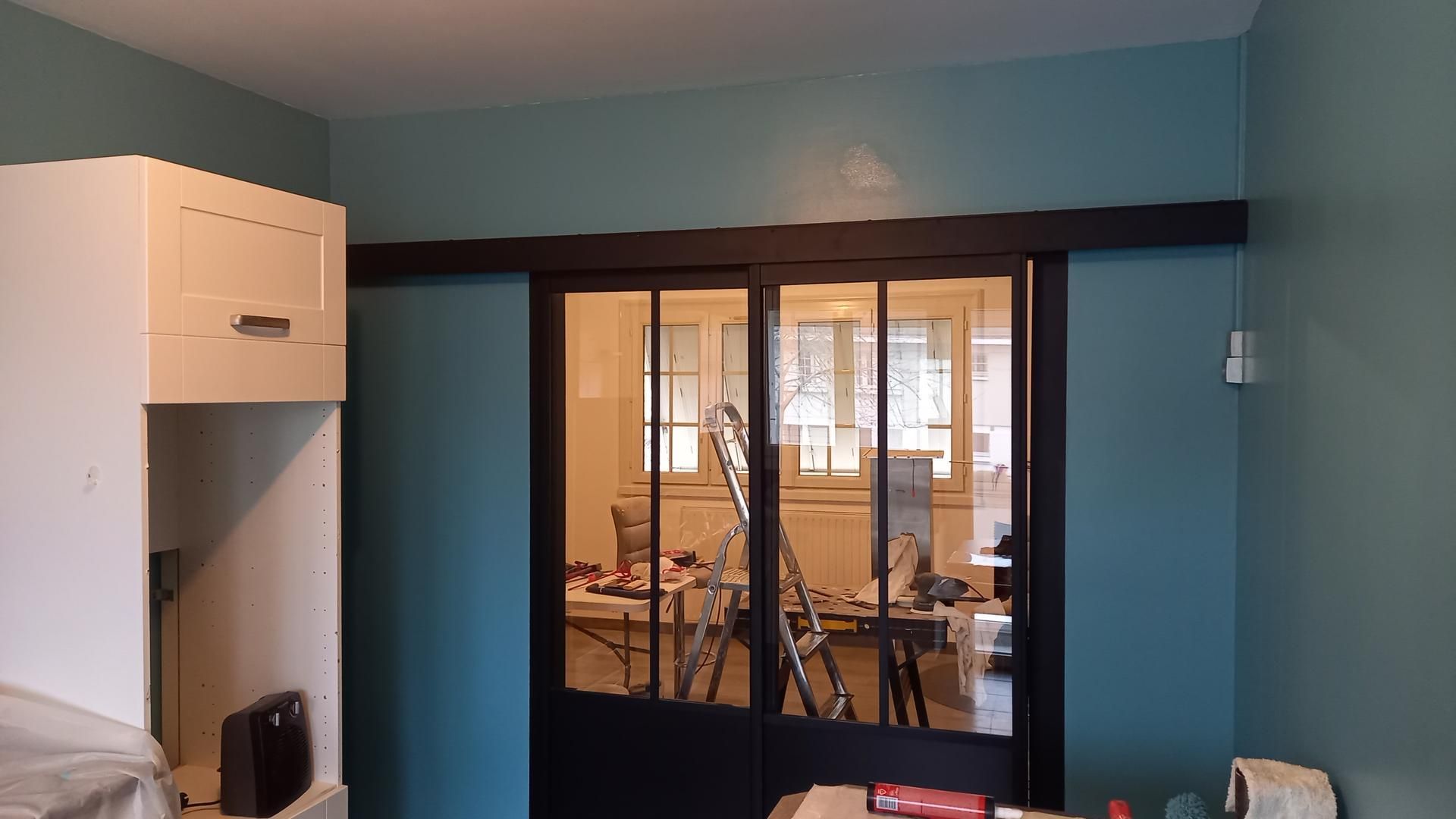 Petite pièce aux murs bleus, aux armoires blanches et aux doubles portes vitrées donnant sur un bureau lumineux.