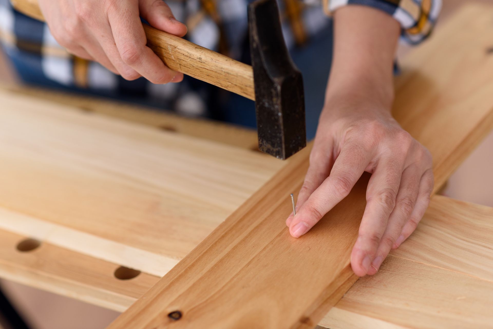 Des mains martelant une planche de bois sur un établi en bois clair.