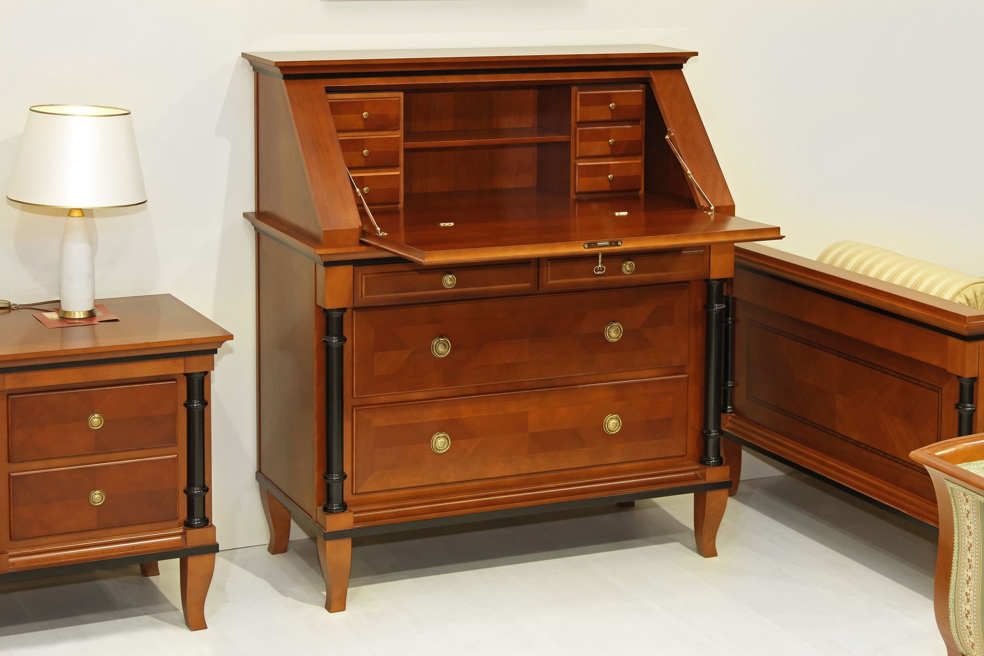Bureau à cylindre en bois flanqué d'une lampe sur une petite table et d'un banc avec un siège rembourré.
