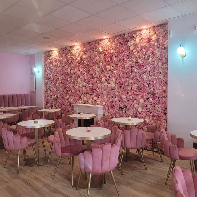 Un restaurante con mesas y sillas rosas y una pared de flores rosas.