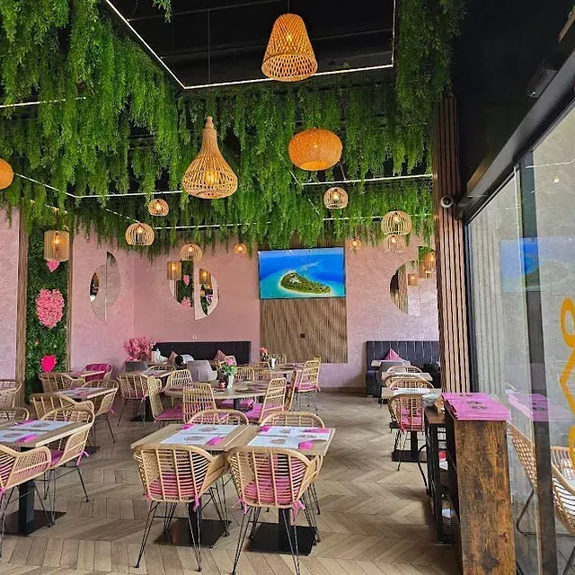 Un restaurante con mesas y sillas y un techo con vegetación colgando de él.