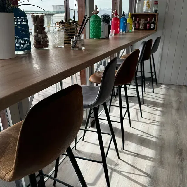 Una fila de taburetes de bar están alineados frente a una larga mesa de madera.