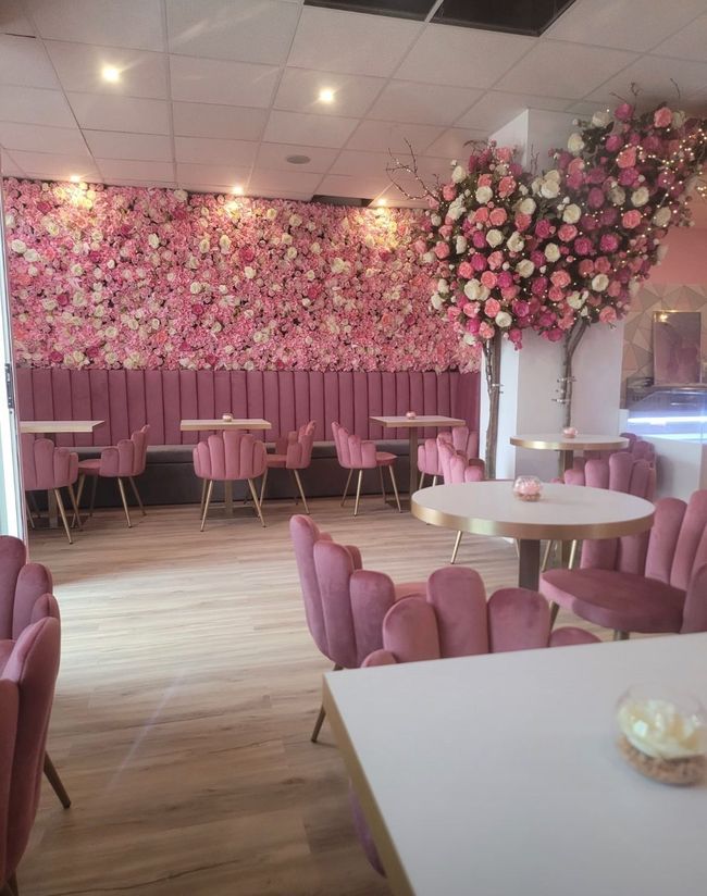 Un restaurante con sillas y mesas rosas y una pared de flores rosas.