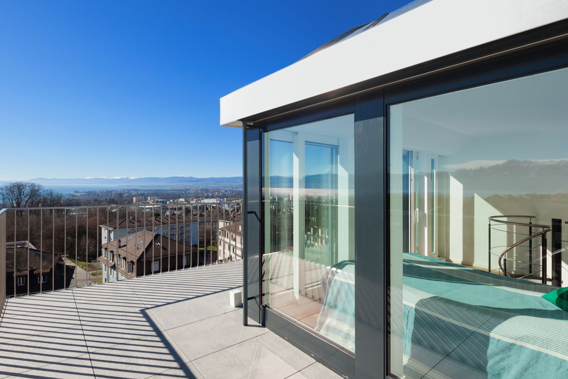 Terrasse moderne sur le toit avec portes coulissantes en verre, vue sur la ville et ciel d'un bleu éclatant.