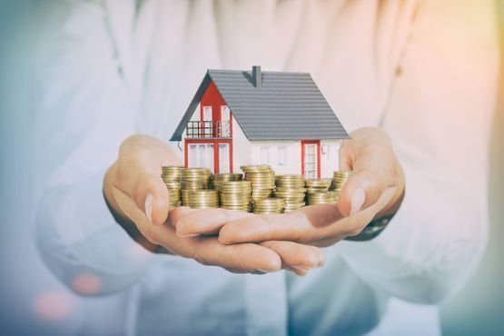 Una persona sostiene una casa modelo y una pila de monedas en sus manos.