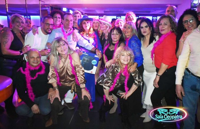 Un numeroso grupo de personas sonríe y posa para una foto de celebración en un local interior muy iluminado.