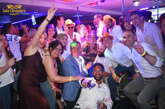 Un grupo de personas con gorros de fiesta y pulseras luminosas sonríen juntas en una discoteca abarrotada.