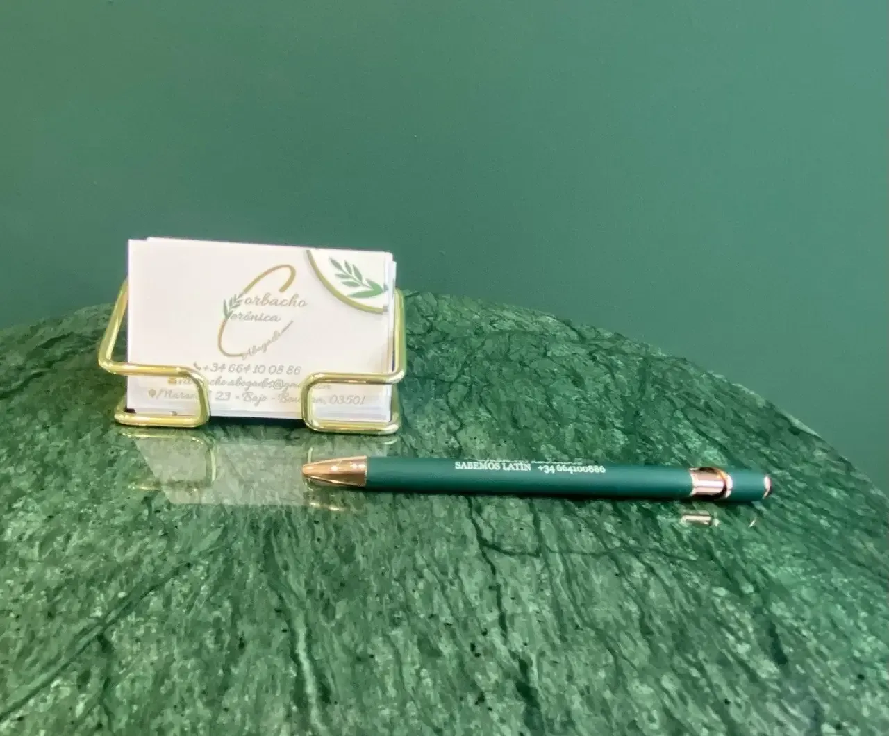 Tarjetas de visita en un soporte dorado y un bolígrafo sobre una superficie de mármol verde sobre un fondo verde.