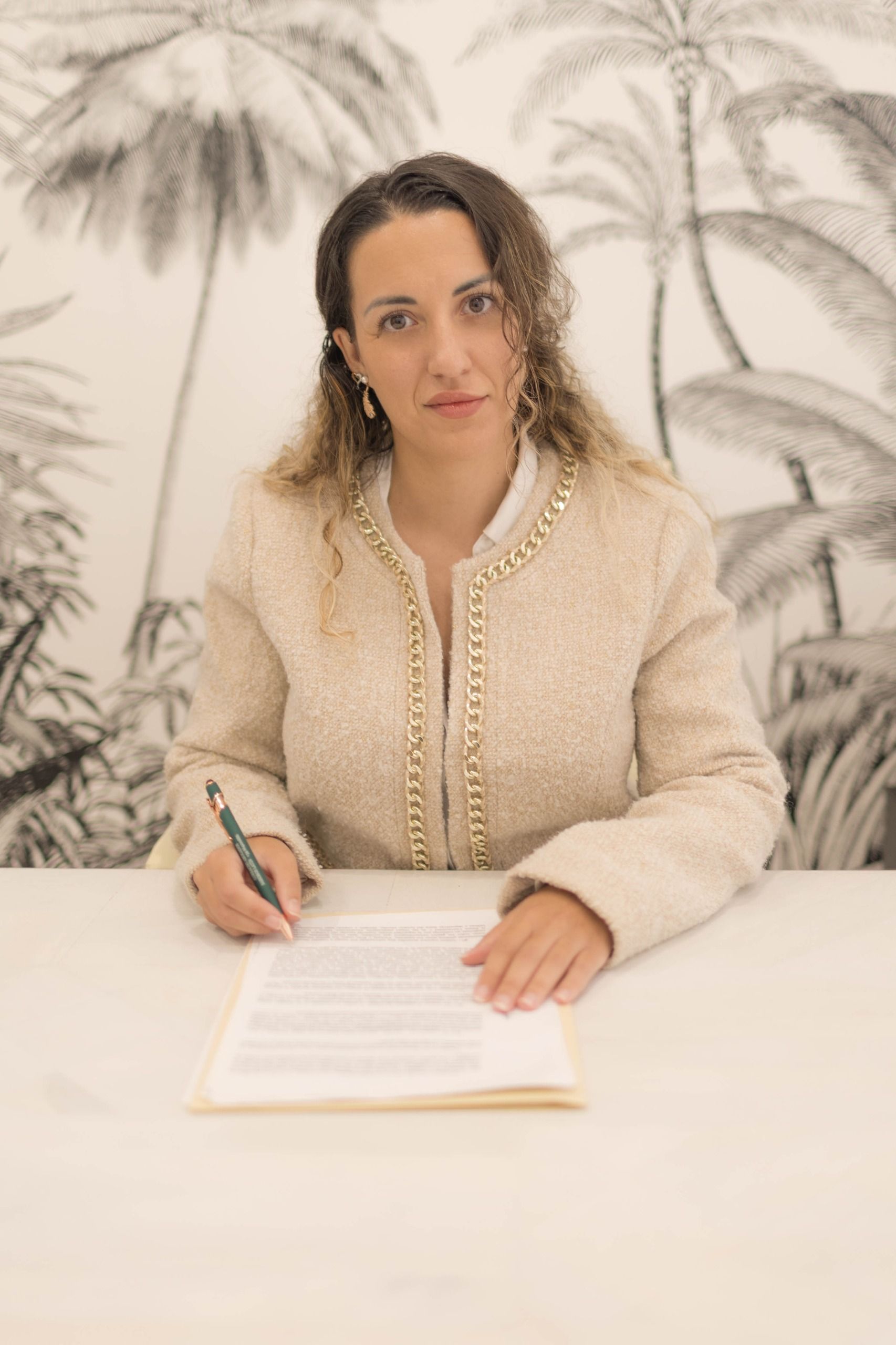 Mujer con blazer verde y hombre con traje en una mesa, mirando documentos.