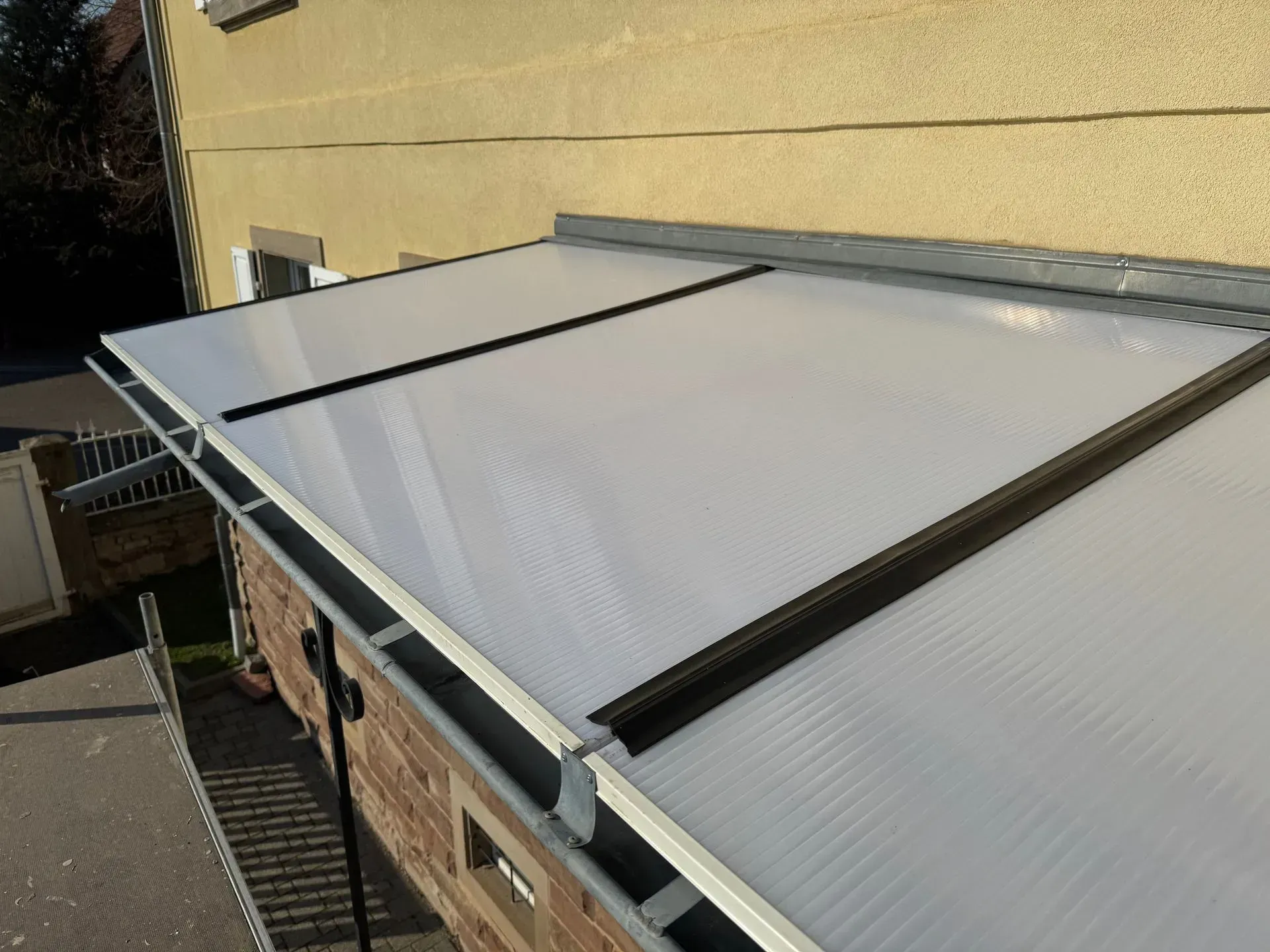 Toiture en polycarbonate recouvrant une structure en briques, vue de dessus, avec gouttières et charpente métallique.