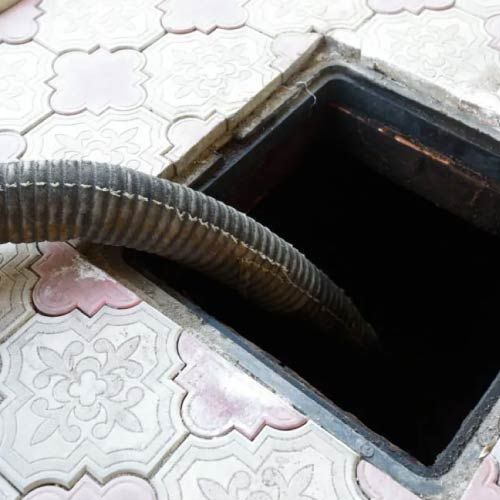 Una manguera sale de una tapa de alcantarilla sobre un piso de baldosas.