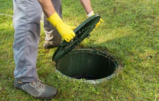 Un hombre que lleva guantes amarillos está abriendo la tapa de un tanque séptico.