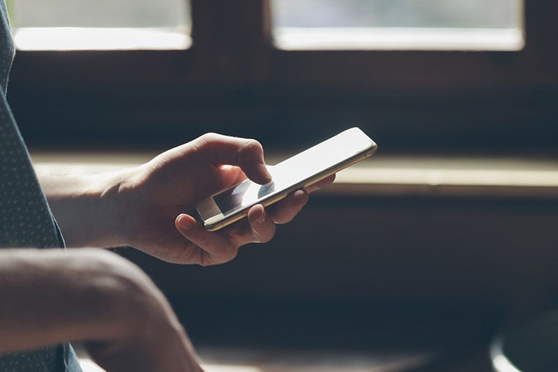 La mano de una persona usando un smartphone, tocando la pantalla con un dedo. El teléfono es dorado.